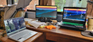 An image of two laptop computers on a desk with a second monitor between them.