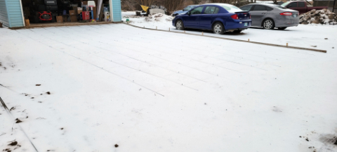 A snow-covered driveway that's prepped for concrete. Rebar is faintly visible under the snow.