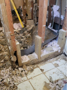 A picture of an exposed interior wall with insulation and other construction debris. The studs do not go all the way to the floor and are connected to short stubby studs.