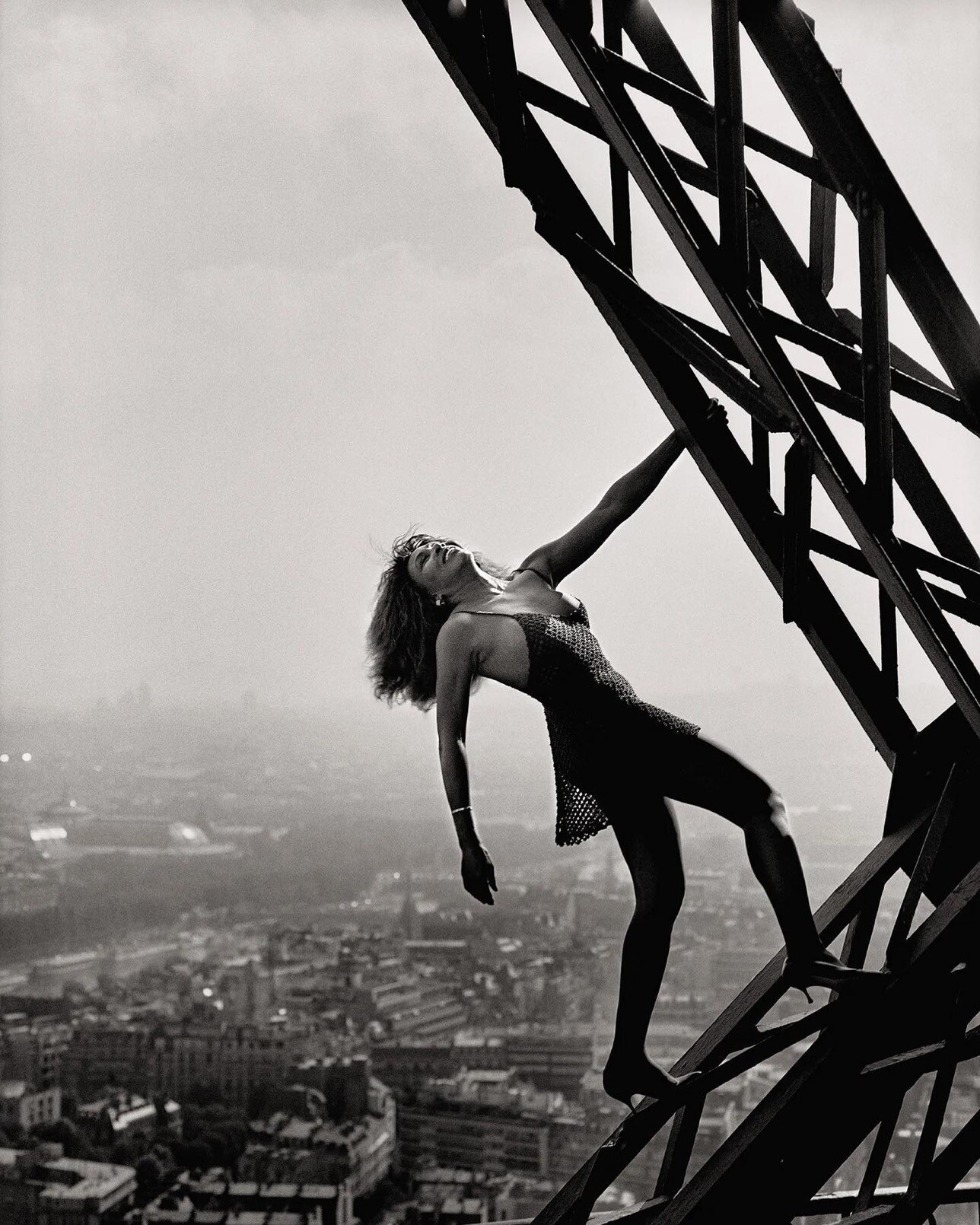 A black and white image of Tina Turner hanging from the Eiffel Tower by Peter Lindbergh