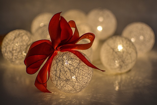 Image of several lighted white Christmas ornaments. The center foreground ornament has a red bow on it.