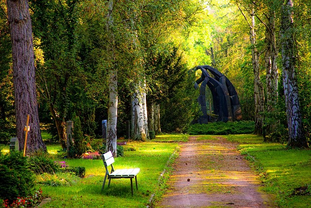 A garden path through a wooded cemetery. There's a dark metal sculpture in teh background. A bench sits on the left side of the path, and several tombstones are visible. |  Homeschooling Isn’t for Everyone—And Neither Is Writing Nice Obituaries