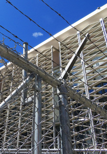 Image of a chain link fence with barbed wire at the top and a secured building behind.