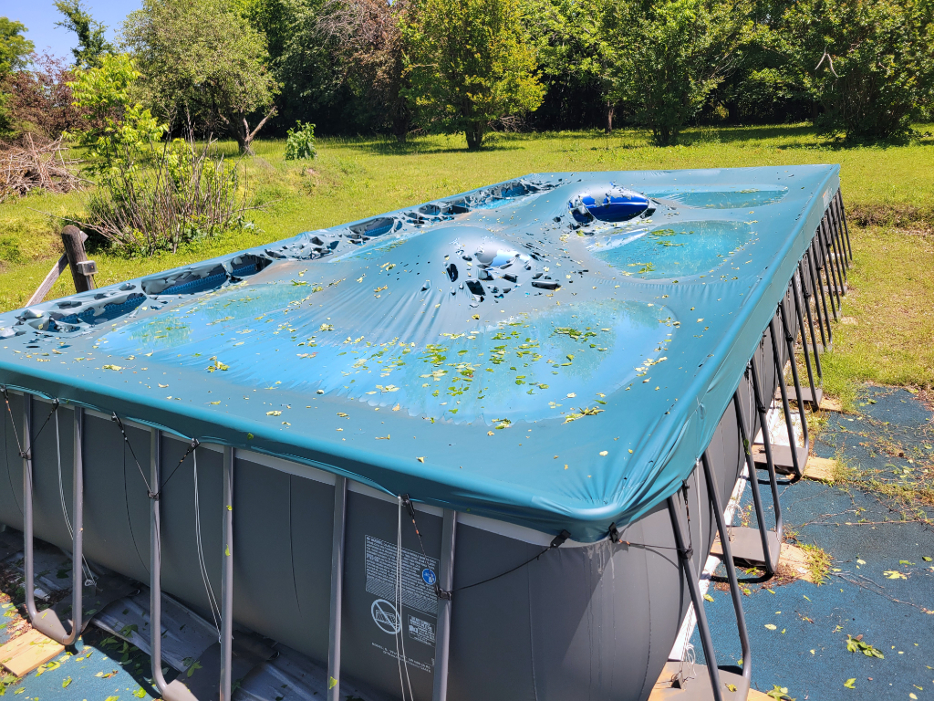 An elevated image of an above-ground pool with a cover damaged by hail. 