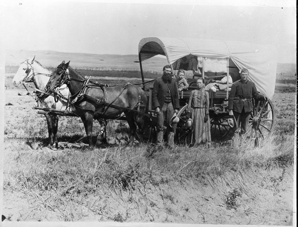 A family standing in front of a covered wagon. | Putting Flesh On The Bones